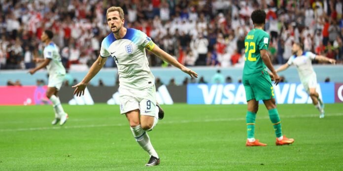 England forward (number 9) celebrates a goal on a green pitch as fans cheer in the stands behind him.