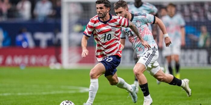 USA soccer player wearing number 10 in red-and-white striped jersey dribbles the ball while a defender pursues.