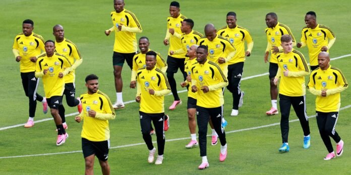 Soccer players in matching yellow training kits jog on a green field during practice.