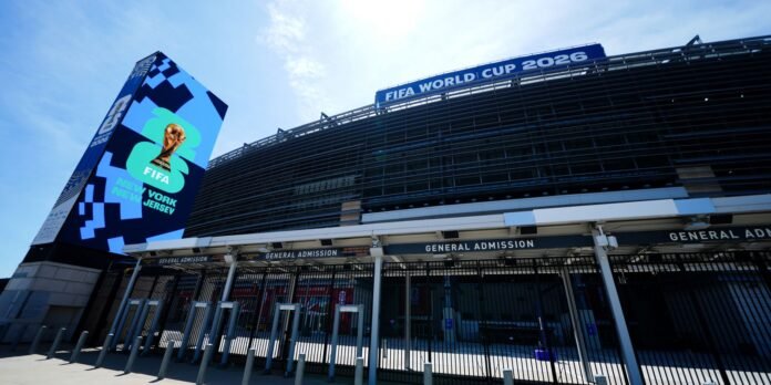 Exterior view of a FIFA World Cup 2026 stadium with a tall blue banner featuring the trophy and 