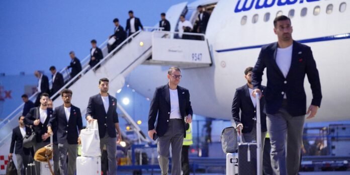 Group of men in blazers walking off a jet onto the tarmac with rolling suitcases and stairs nearby, after deplaning on a clear evening