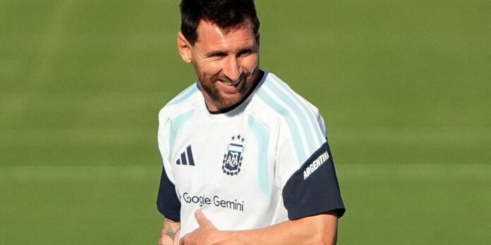 Argentine footballer in white and light-blue training jersey, smiling on a green pitch.