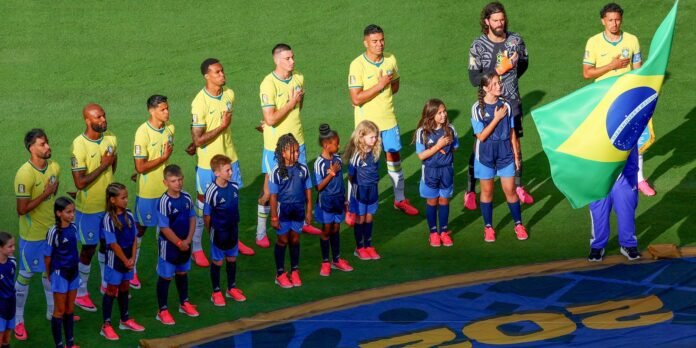 Brazilian national team players in yellow jerseys stand with children on a football field, hands over their hearts.”