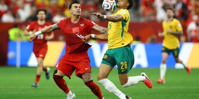 Two soccer players clash for the ball mid-air, one in a red Turkey kit and the other in a yellow-green Brazil kit, on a green field with a blurred crowd behind.