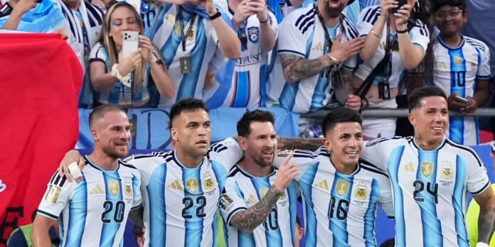 Argentina national football team players pose together with fans after a match, arms around shoulders in a celebratory moment behind a blue and white banner.