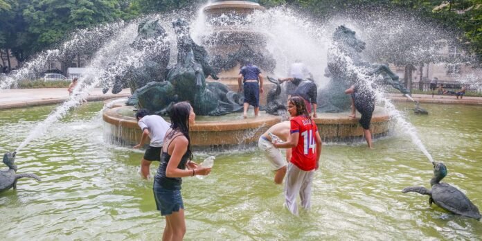 Children play and splash in a circular park fountain with water jets spraying from bronze statues.