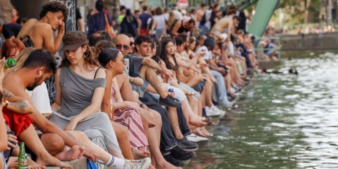 Crowd of people sitting along a riverside promenade, feet over the water, chatting and relaxing.