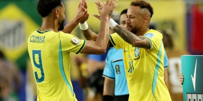 Two Brazilian football players in yellow jerseys celebrate on the field, high-fiving each other in celebration.