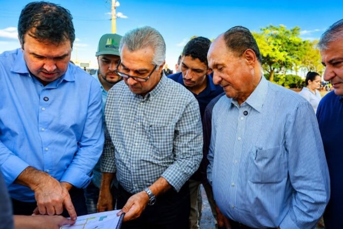 Group of men in casual shirts huddled together outdoors, studying a map or document laid on a table.