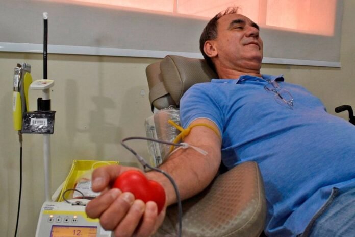 Man reclining in a chair donating blood, holding a red heart-shaped ball in his hand.