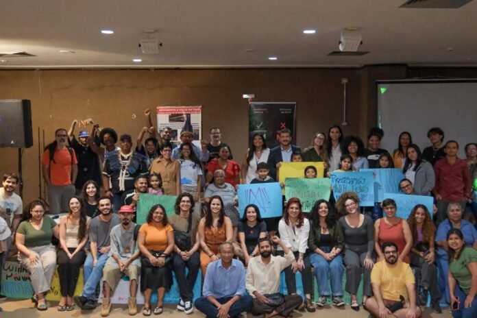 Large diverse group of people posing for a group photo in a conference room, some holding colorful signs.