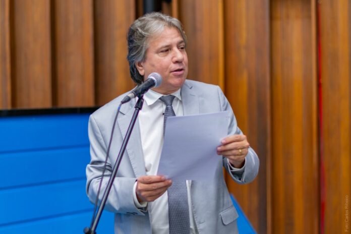 Man in a light gray suit speaks into a microphone while holding papers