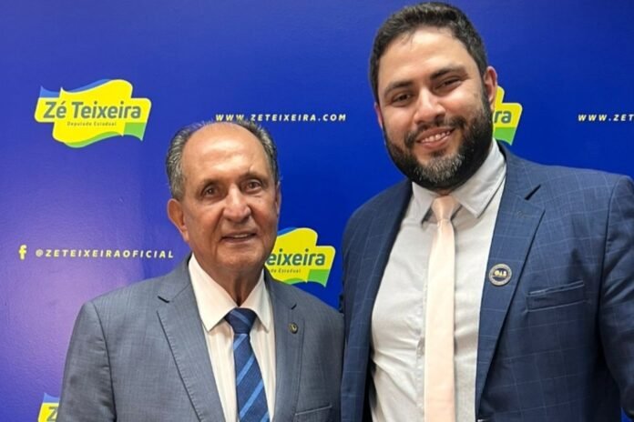 Two men in suits pose for a photo in front of a blue campaign backdrop with Ze Teixeira branding.