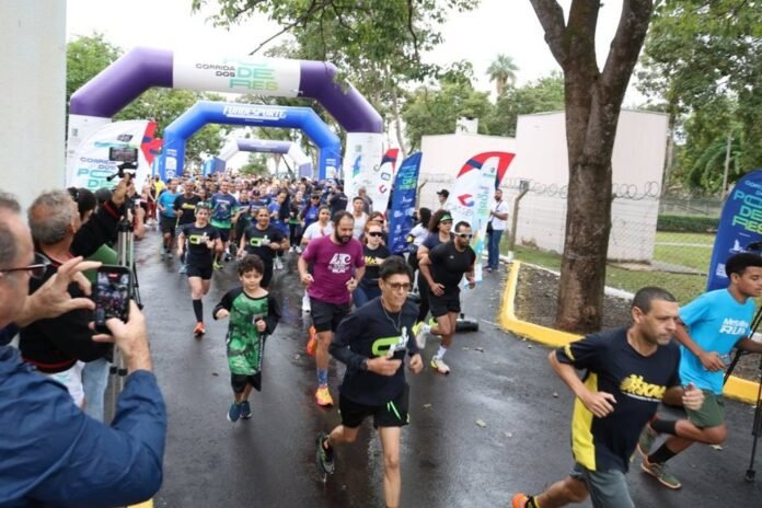 Runners start a race on a wet street as a crowd cheers, with purple inflatable arches and sponsor banners overhead.