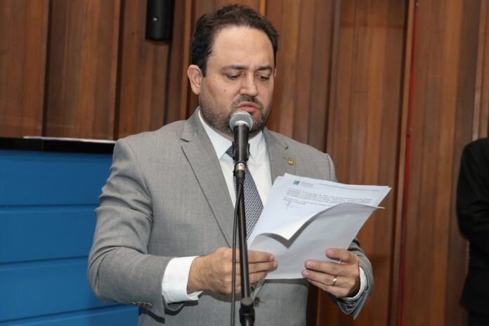 Man in a gray suit reads from papers into a microphone during a formal speech.