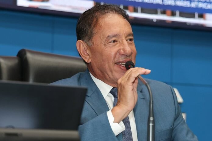 Man in a blue suit speaks into a microphone at a panel discussion or conference.