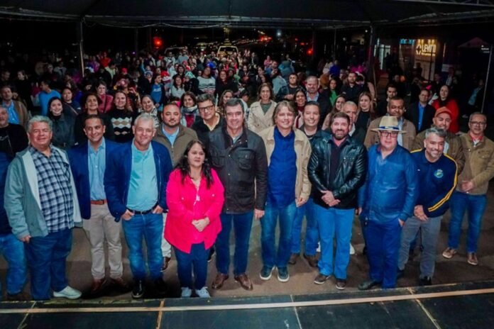 Large diverse group of people posing for a group photo on a stage under a tent at an outdoor night event.
