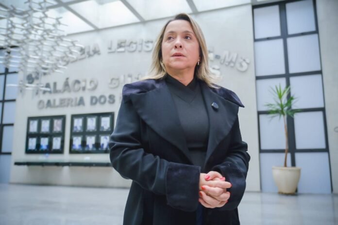 Professional woman in a dark coat stands in a modern atrium, hands clasped, looking ahead.