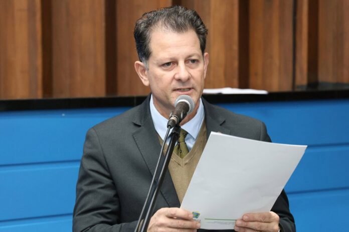 Man in a suit speaks into a microphone while holding a sheet of paper.