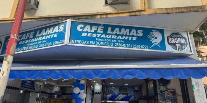 Storefront of Café Lamas Restaurante with a blue sign and scalloped blue awning, festive blue/white balloons inside the entrance.