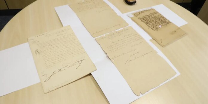 Several aged handwritten letters laid out on a round light wooden table, with white mounting strips beneath them