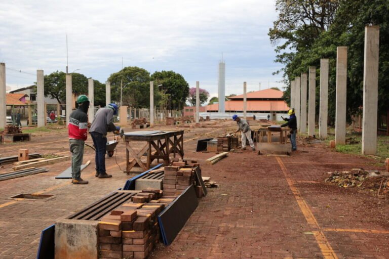Construction site with workers laying bricks on a brick-paved area, with bricks and building materials nearby.