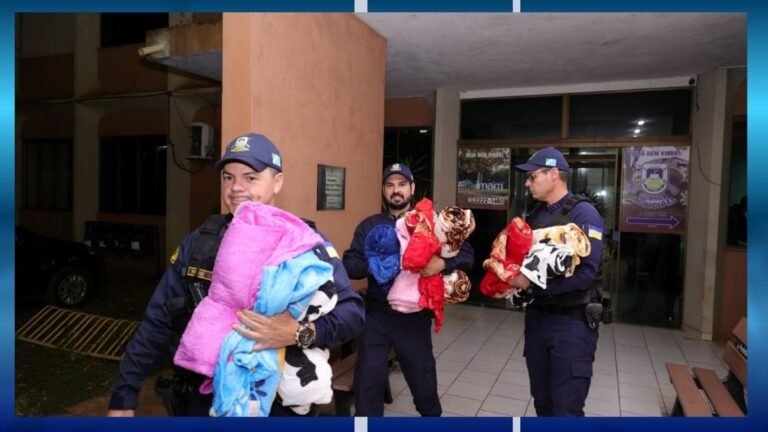 Uniformed officers carry and distribute bundled blankets outside a building entrance at night/evening.