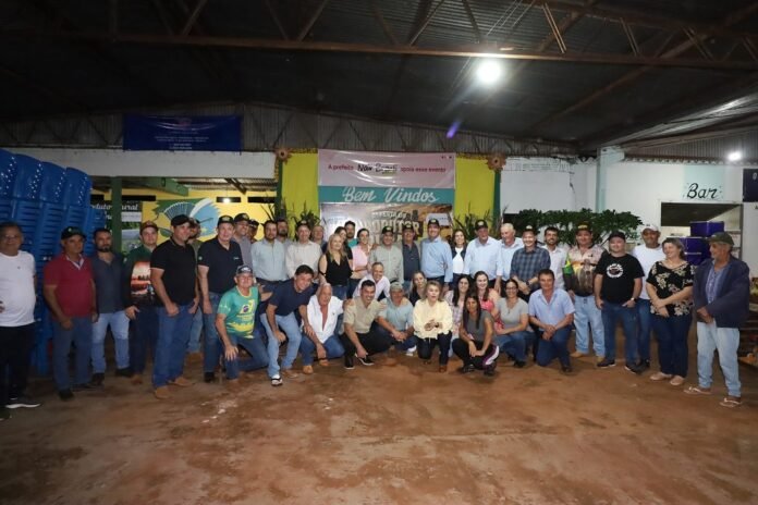 Large group of people posing for a group photo at an indoor community event, with banners and a bright yellow backdrop in the background.