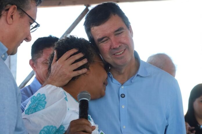 Two people share a tender moment: a woman holds a microphone while leaning on a smiling man during an event.”,
