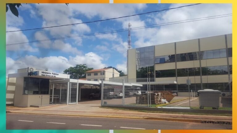 Front view of the Ministério Público building behind a tall fence with a gated entrance and parked cars nearby.