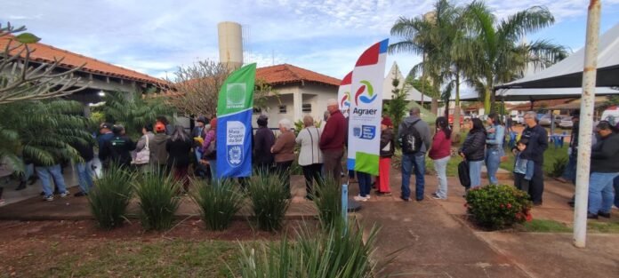 People line up at an outdoor community event with banners and palm trees nearby.