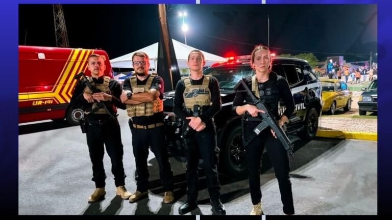 Four armed security personnel in tactical vests stand in front of a black SUV at a nighttime event.