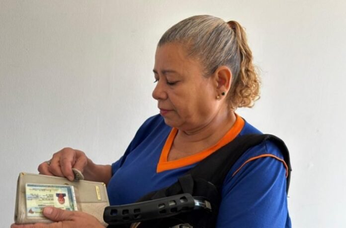 Woman in a blue uniform with orange trim looks into a wallet, inspecting a card inside.