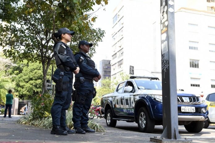 Two police officers in dark uniforms standing guard beside a blue and white police pickup on a city street.