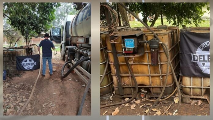 Man in a blue shirt and jeans stands beside a large white fuel tanker truck, with hoses on the ground and a police banner nearby in a yard.