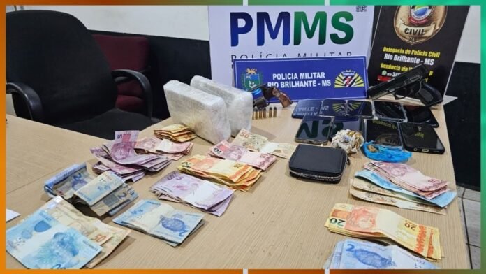 Table with seized items: stacks of Brazilian currency, white bricks (drugs) and a handgun, with police signs in the background—evidence of a drug arrest by PMMS Rio Brilhante MS