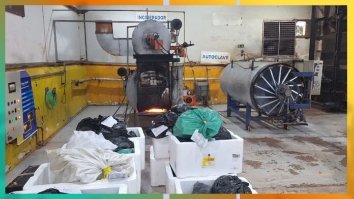 Industrial waste processing room with an incinerator firing flames; large autoclave to the right and labeled signs nearby (Incinerador, Autoclave).