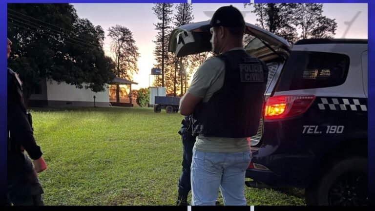 Police officers near an open car trunk at dusk, one wearing a tactical vest and jeans, in a grassy area.