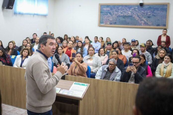 Man speaking into a microphone at a lectern in a crowded meeting room.
