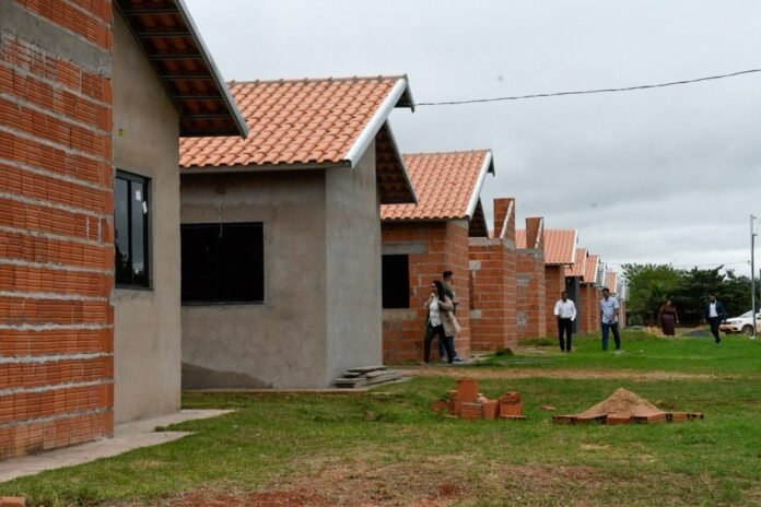 Row of brick houses under construction with orange-tiled roofs and people walking along the site.