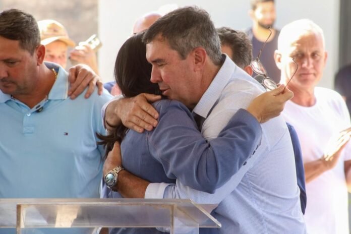 Two people share a warm hug at a crowd event, with onlookers in the background.