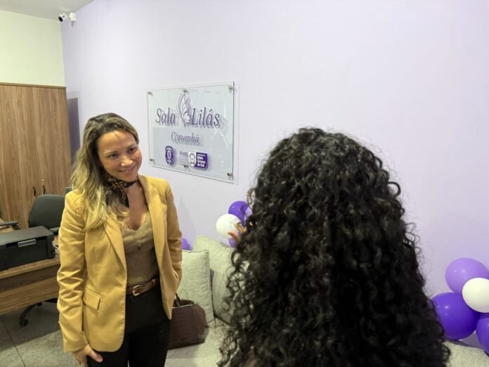 Two women talking in a lavender office with purple and white balloons; a wall sign reads 'Sada Lilás'.