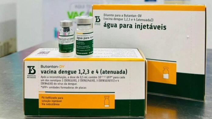 Dengue vaccine boxes and small vials on a lab counter, labeled água para injectáveis (injection water).