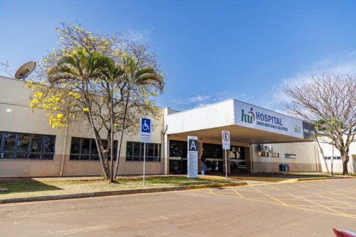 Exterior of a university hospital with a covered entrance, a wheelchair-accessible sign, and a palm tree in front.