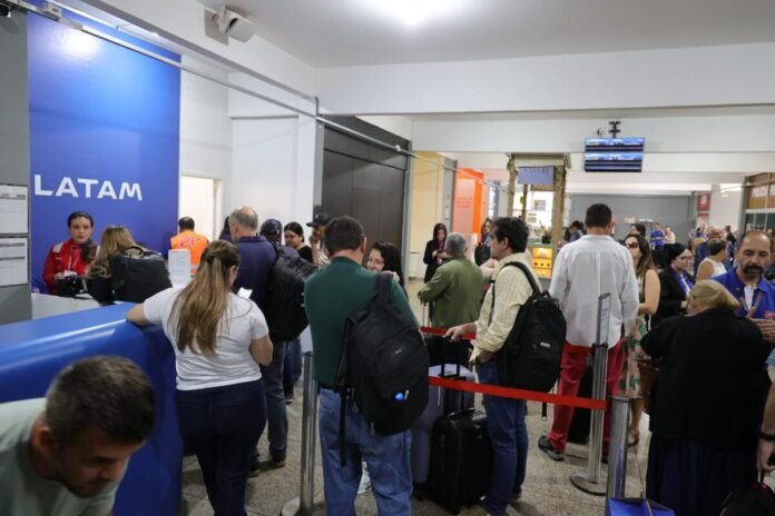 Airport check-in area for LATAM with a long queue of passengers and staff at the counter, luggage on the floor and reusable barriers guiding the line.