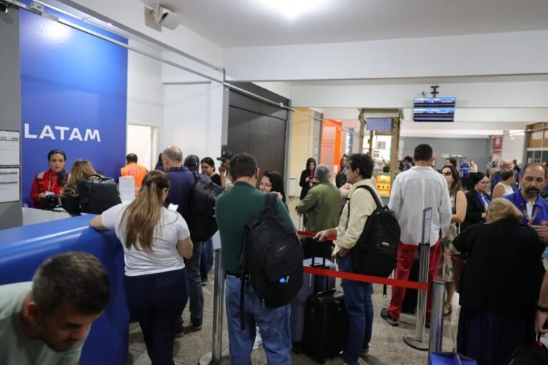 Airport check-in area for LATAM with a long queue of passengers and staff at the counter, luggage on the floor and reusable barriers guiding the line.