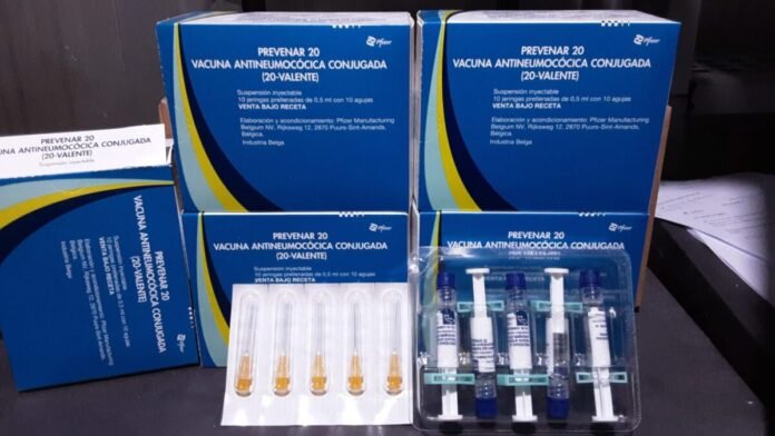 Six blue boxes labeled Prevenar 20 vaccine with a blister pack of syringes and vials in front.