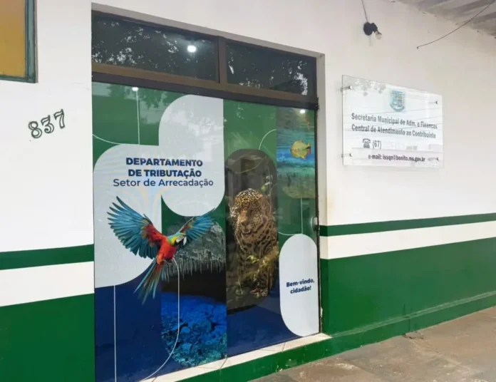 Entrance to the Department of Taxation (Setor de Arrecadação) in a municipal building, with a colorful parrot mural on the door and a jaguar visible inside behind glass.
