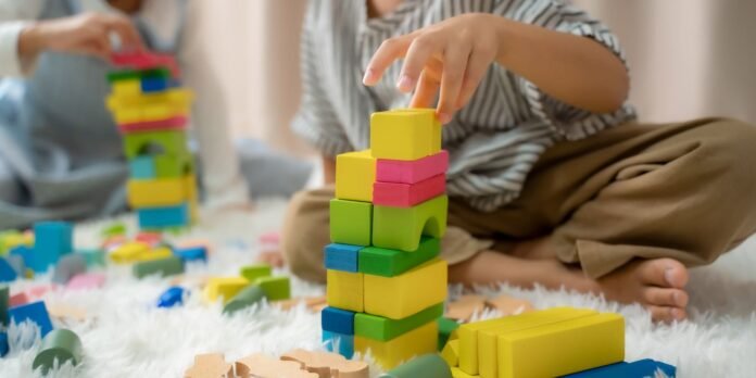 Child stacks a tall tower of colorful wooden blocks on a fluffy rug during playtime.