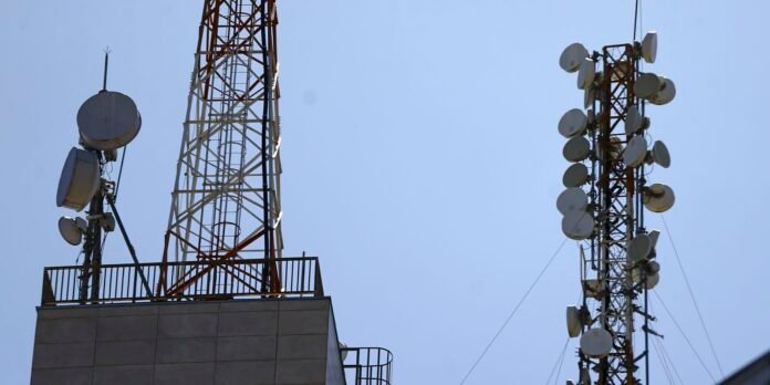 Cell towers with numerous satellite dishes and antennas against a clear blue sky, infrastructure for wireless communication.